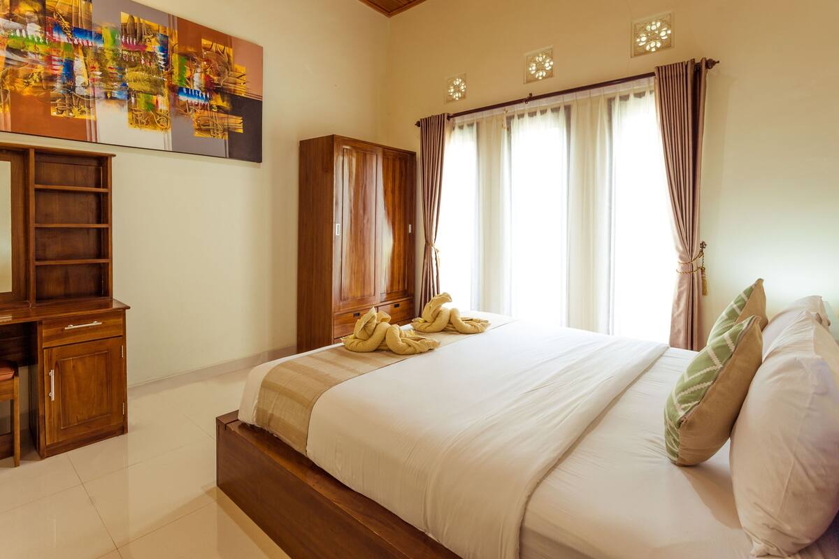 A neatly made bed with a wooden headboard, a bedside table with a lamp, and a large abstract painting on the wall.