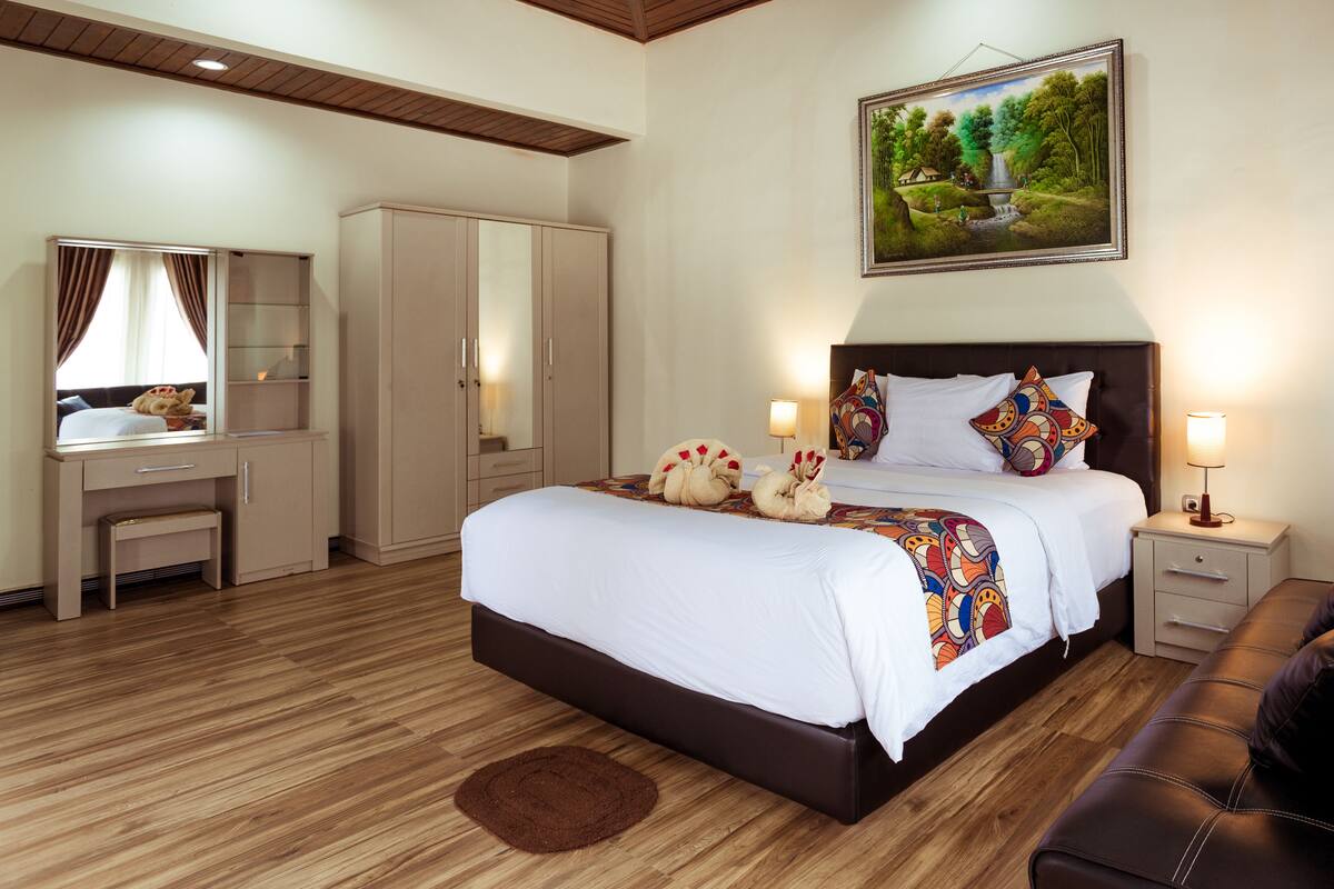 A hotel room with a large bed, a desk, a wardrobe, and a painting on the wall.
