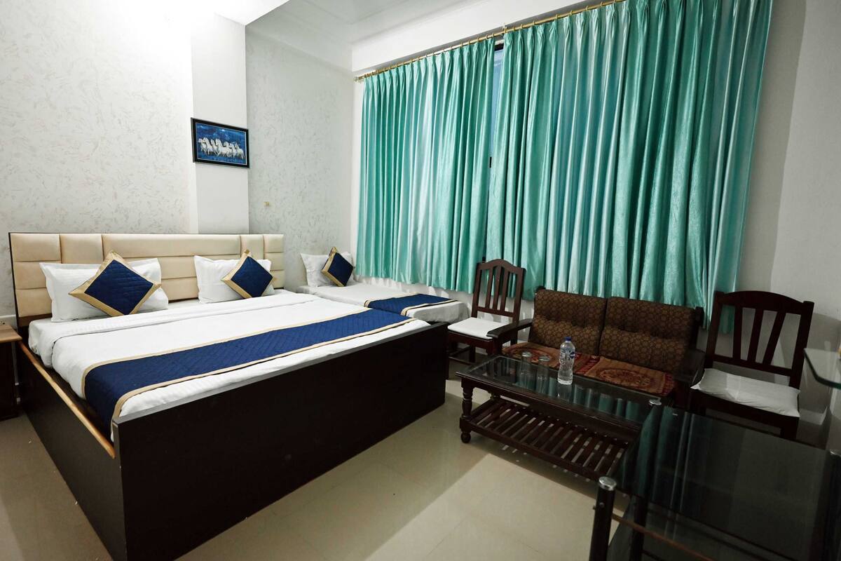 Une chambre d’hôtel avec un grand lit, deux chaises, une petite table et des rideaux de couleur turquoise.
