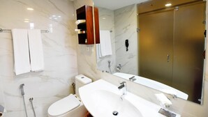 A modern bathroom with a marble wall, a large mirror, a sink, a toilet, and a shower. - Viridi Hotels (Islamabad)