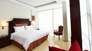 A hotel room with a large bed, a nightstand with a phone, a chair, and a window with curtains. - Viridi Hotels (Islamabad)