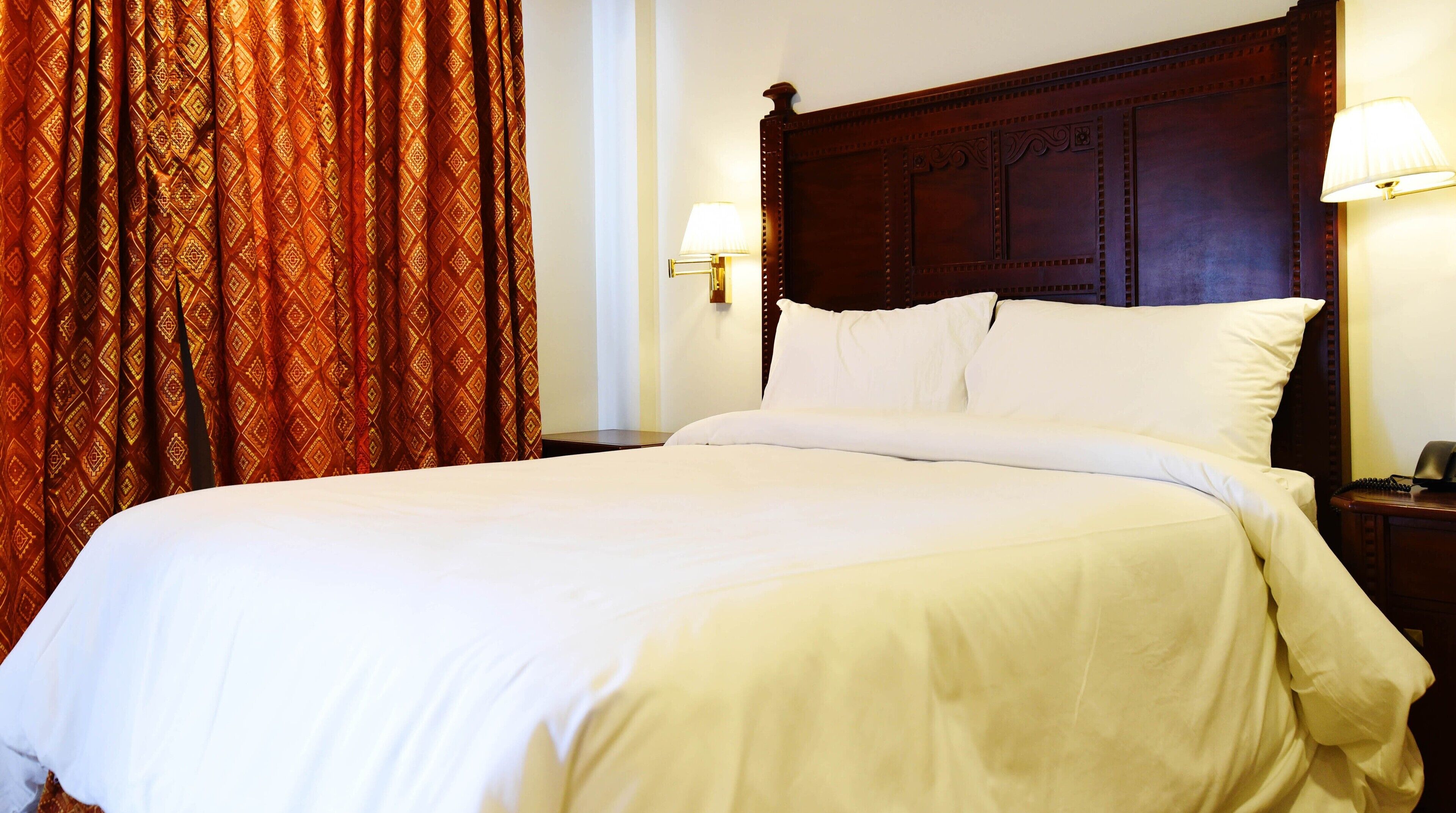 A neatly made bed with white linens, a wooden headboard, and two bedside lamps.