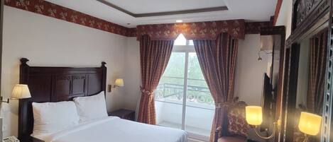 A hotel room with a large bed, a desk with a chair, a small table with a tray, and a large mirror.