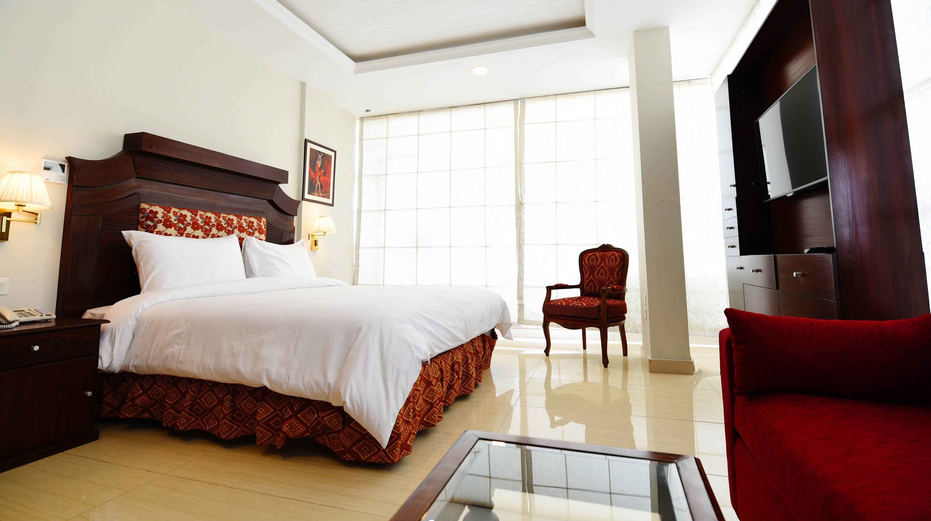A hotel room with a large bed, a chair, a TV, and a glass table.