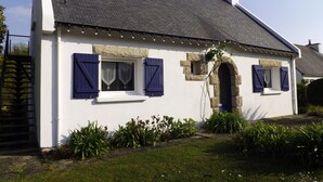 A white cottage with a grey roof, stone window frames, and blue shutters. - Independent dwelling in 1 detached house near sea. (GUIDEL)
