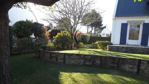 A well-maintained garden with a stone wall, a lawn, and a variety of trees and shrubs. - Independent dwelling in 1 detached house near sea. (GUIDEL)