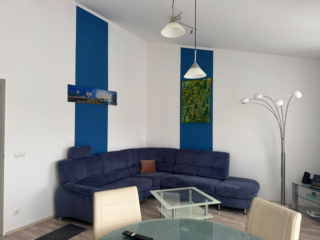 A modern living room with a blue sectional sofa, a glass coffee table, and a white pendant light.