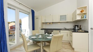 A modern kitchen with a dining area, featuring a glass table, beige chairs, and a view through the glass door. - Renovated vacation apartment Mare - Holiday apartment Mare in Zinnowitz (Zinnowitz)
