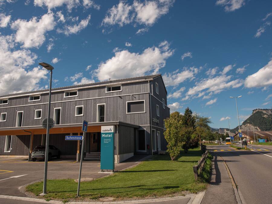 A modern building with a sign for a motel, a parking area, and a road with a bus.