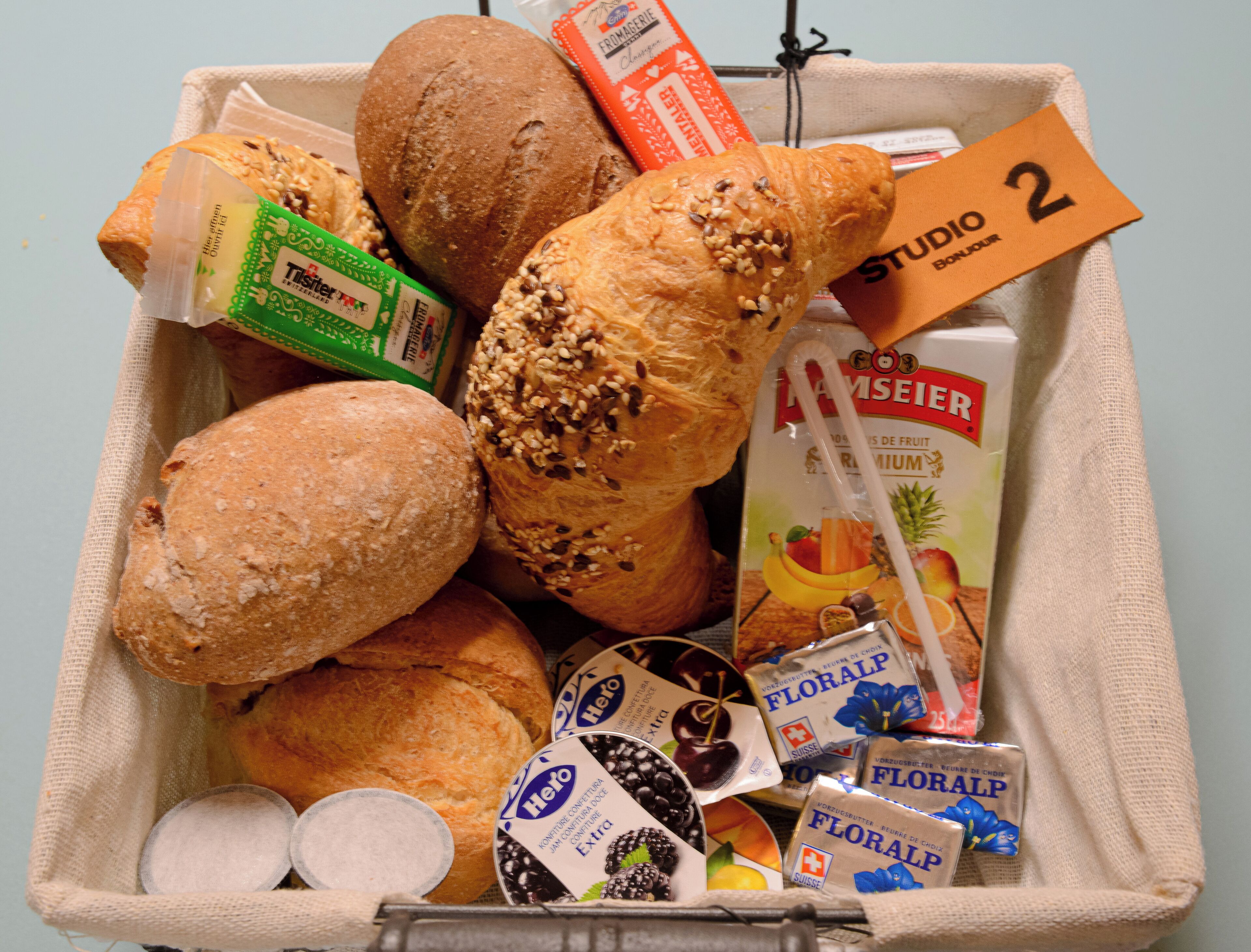 Eine Auswahl an Brot und Gebäck in einem Korb, darunter eine Baguette, ein Croissant und ein Laib Brot.