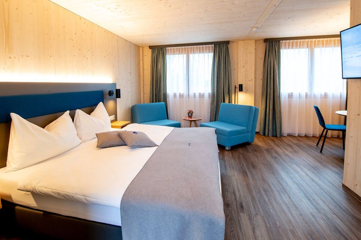A hotel room with a large bed, two armchairs, a small table, and a TV.