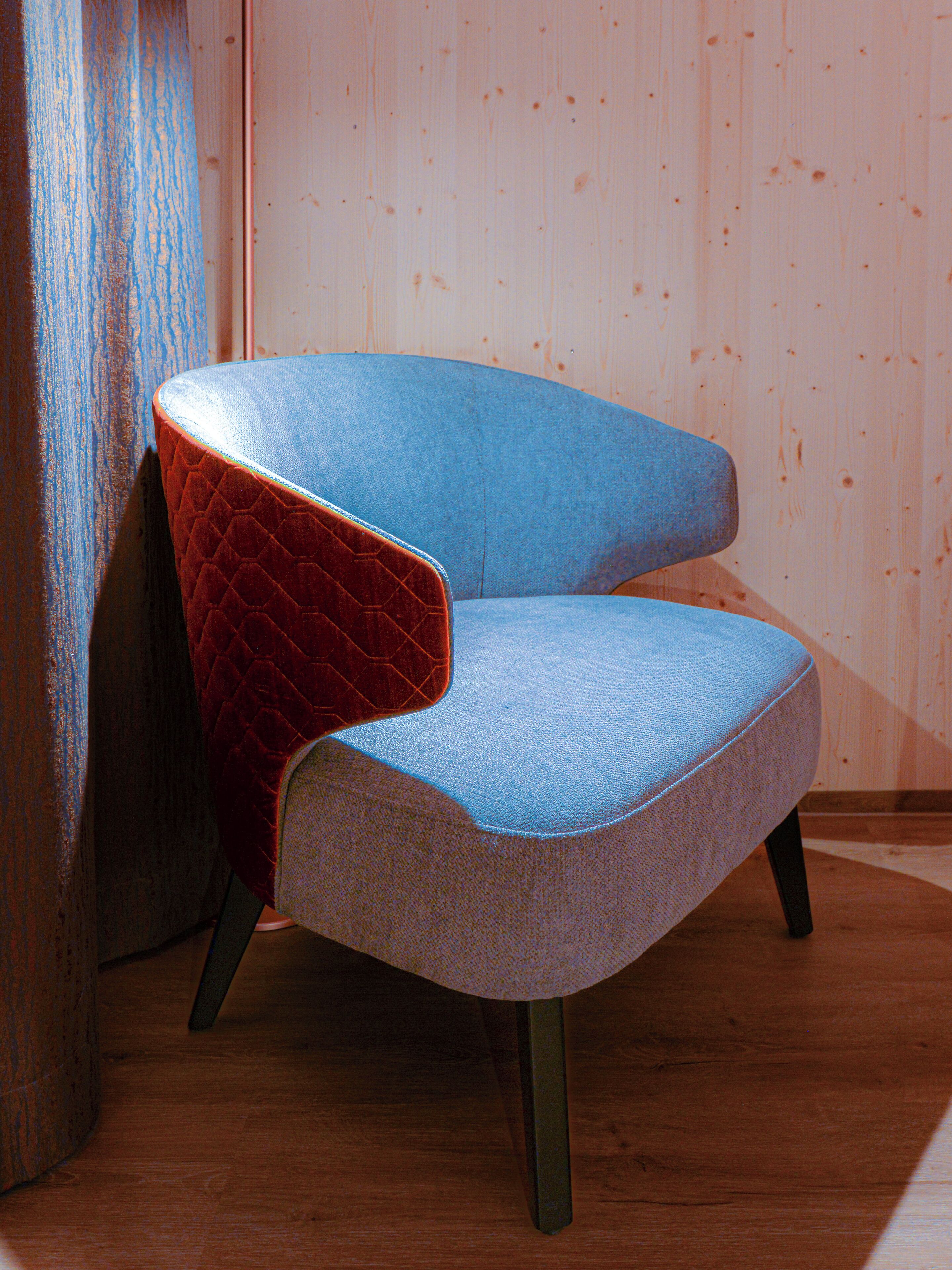 Una silla con respaldo rojo y asiento azul, ubicada frente a una pared de madera.