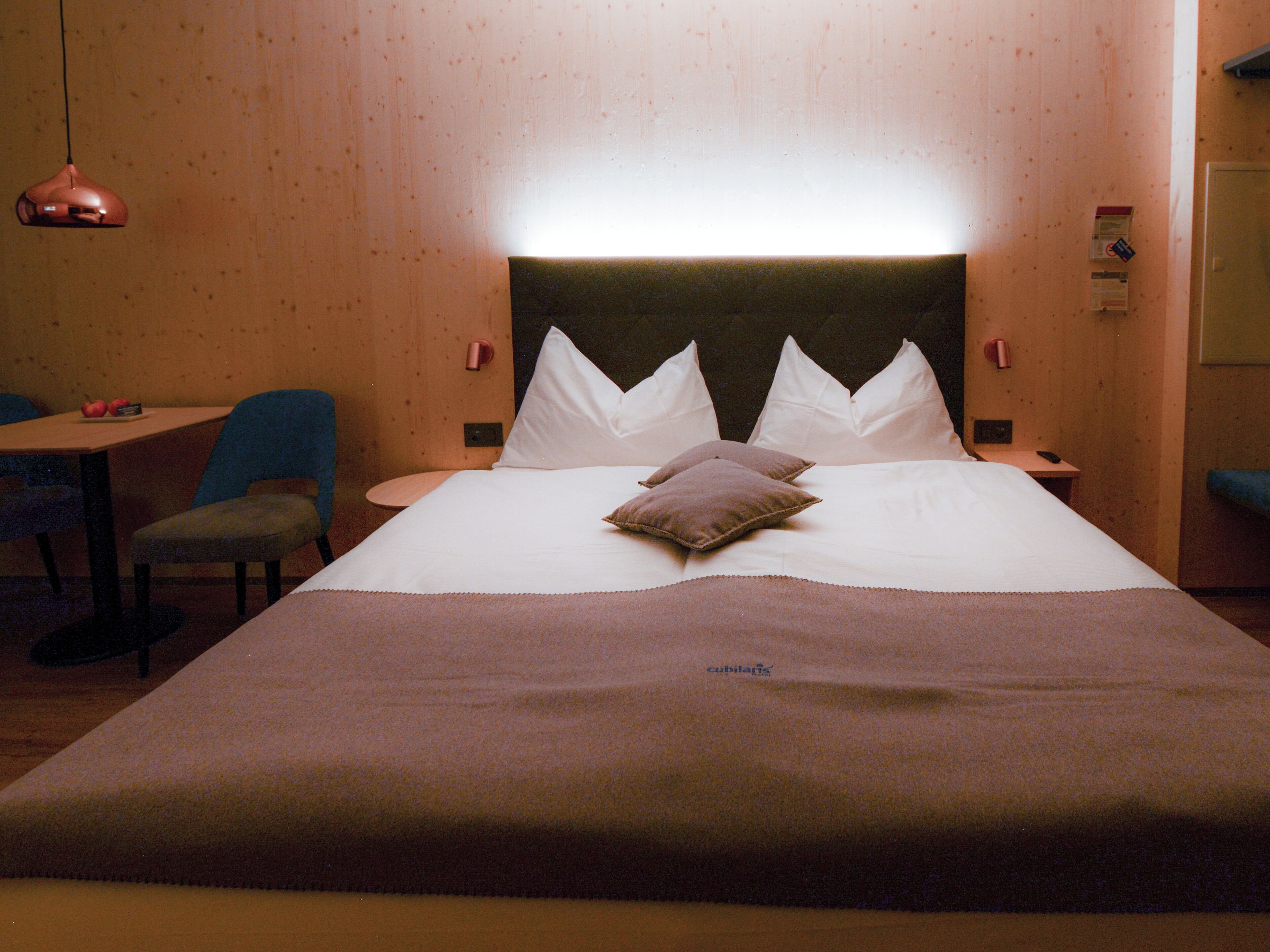 A hotel room with a large bed, two pillows, a bedside table, a chair, and a lamp.