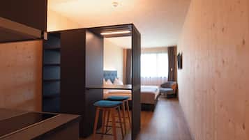 A modern hotel room with a wooden interior, a bed, a desk, and two bar stools.