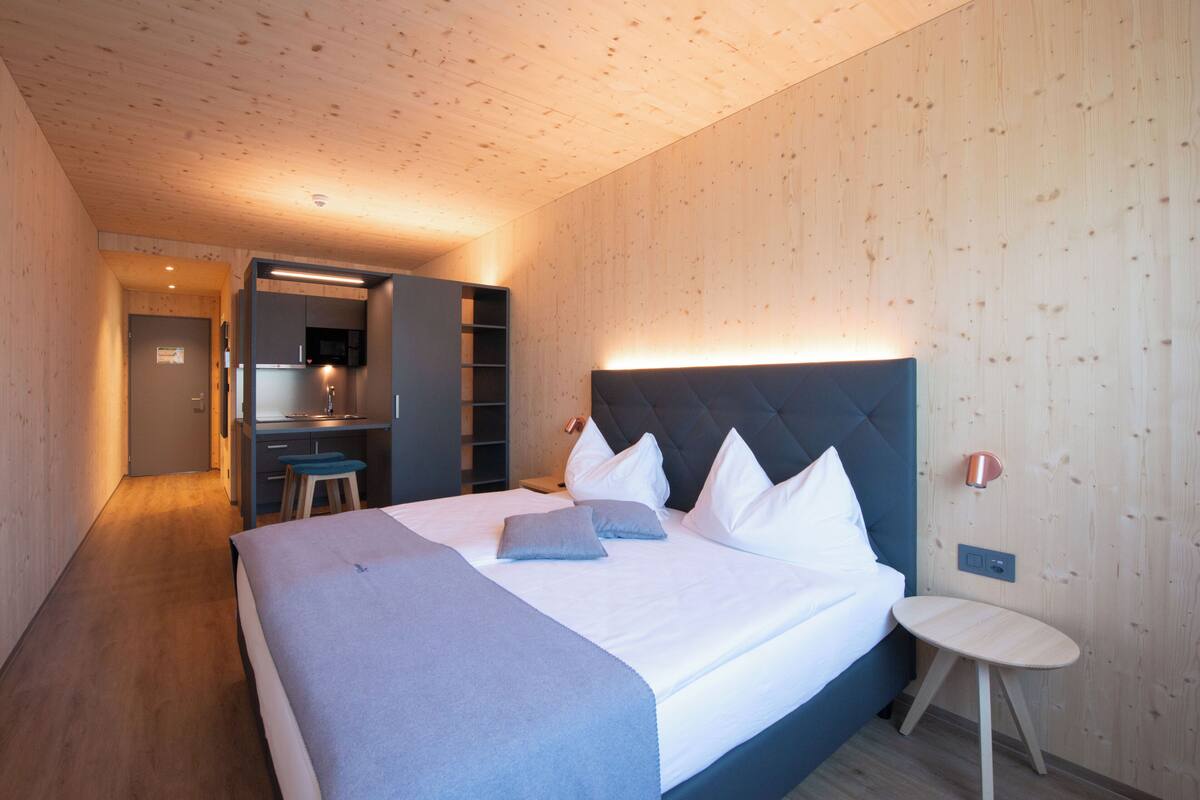 A modern hotel room with a large bed, a small desk, and a built-in wardrobe.