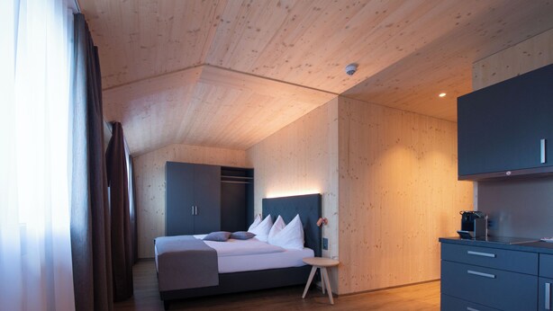 A modern hotel room with a wooden ceiling, a bed with white bedding, a small bedside table, and a built-in wardrobe. - Cubilaris Motel Bad Ragaz (Bad Ragaz)