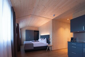 A modern hotel room with a wooden ceiling, a bed with white bedding, a small bedside table, and a built-in wardrobe.