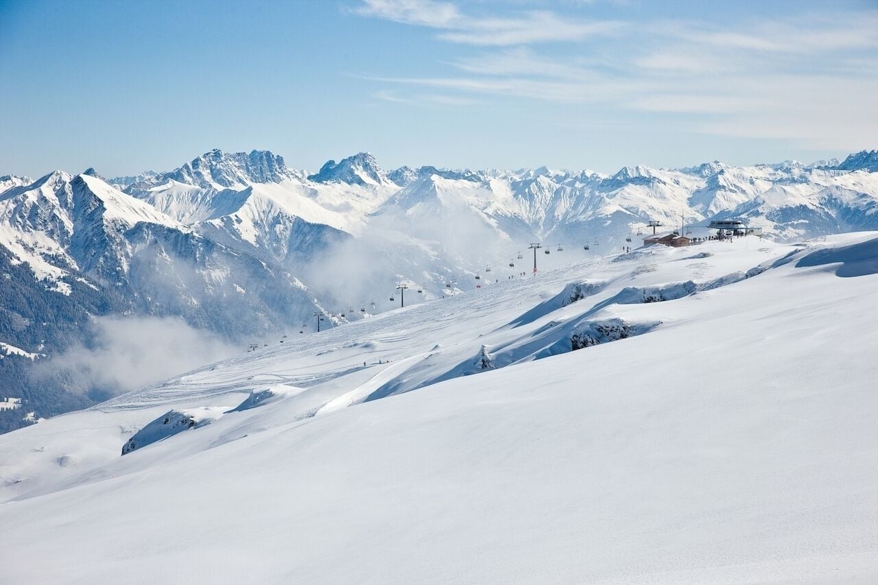 A snow-covered mountain landscape with ski slopes, ski lifts, and a small building likely serving as a lodge or rest area.