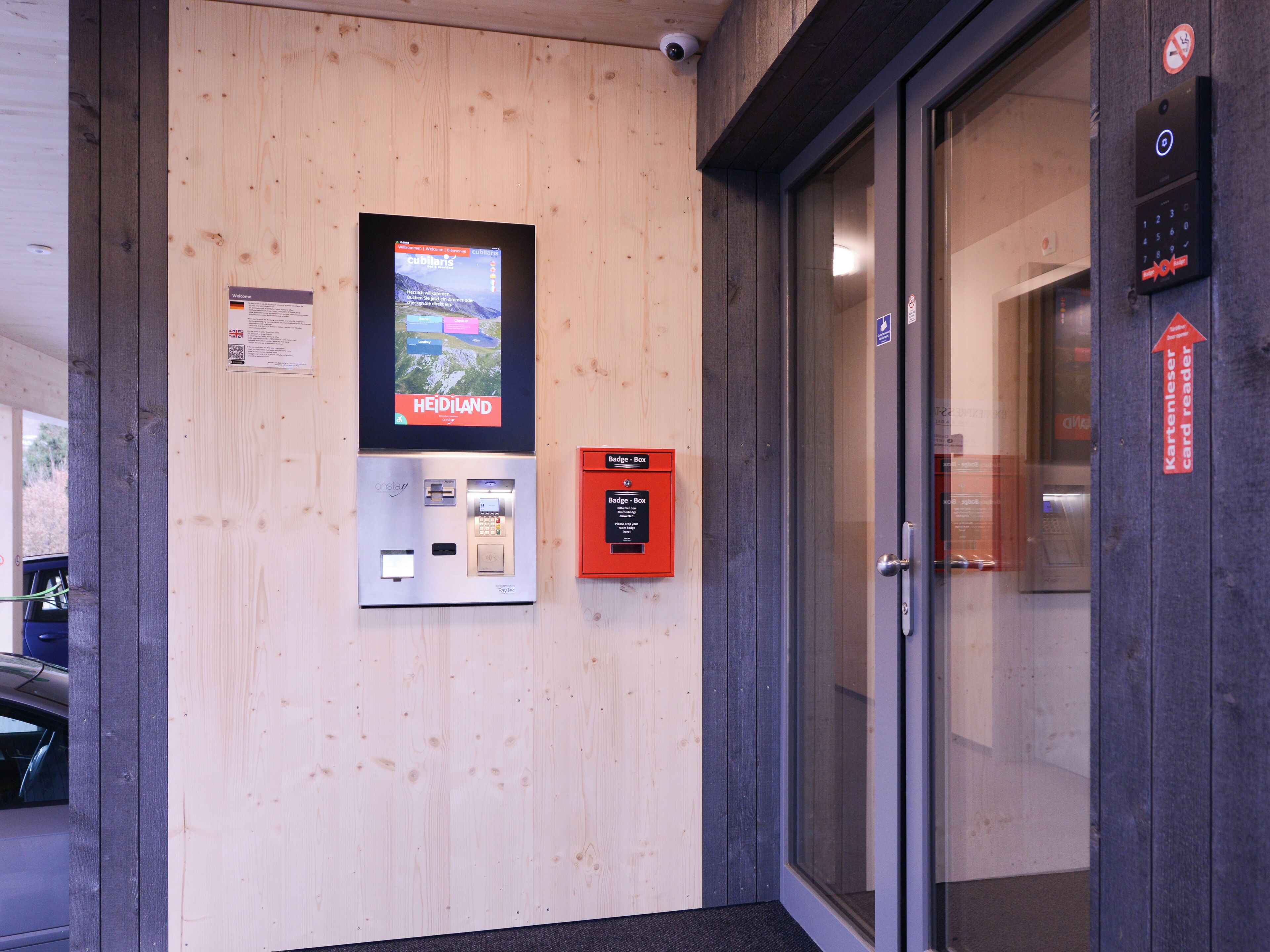 A wooden wall with a digital display, a PayTec machine, a badge box, and a card reader.