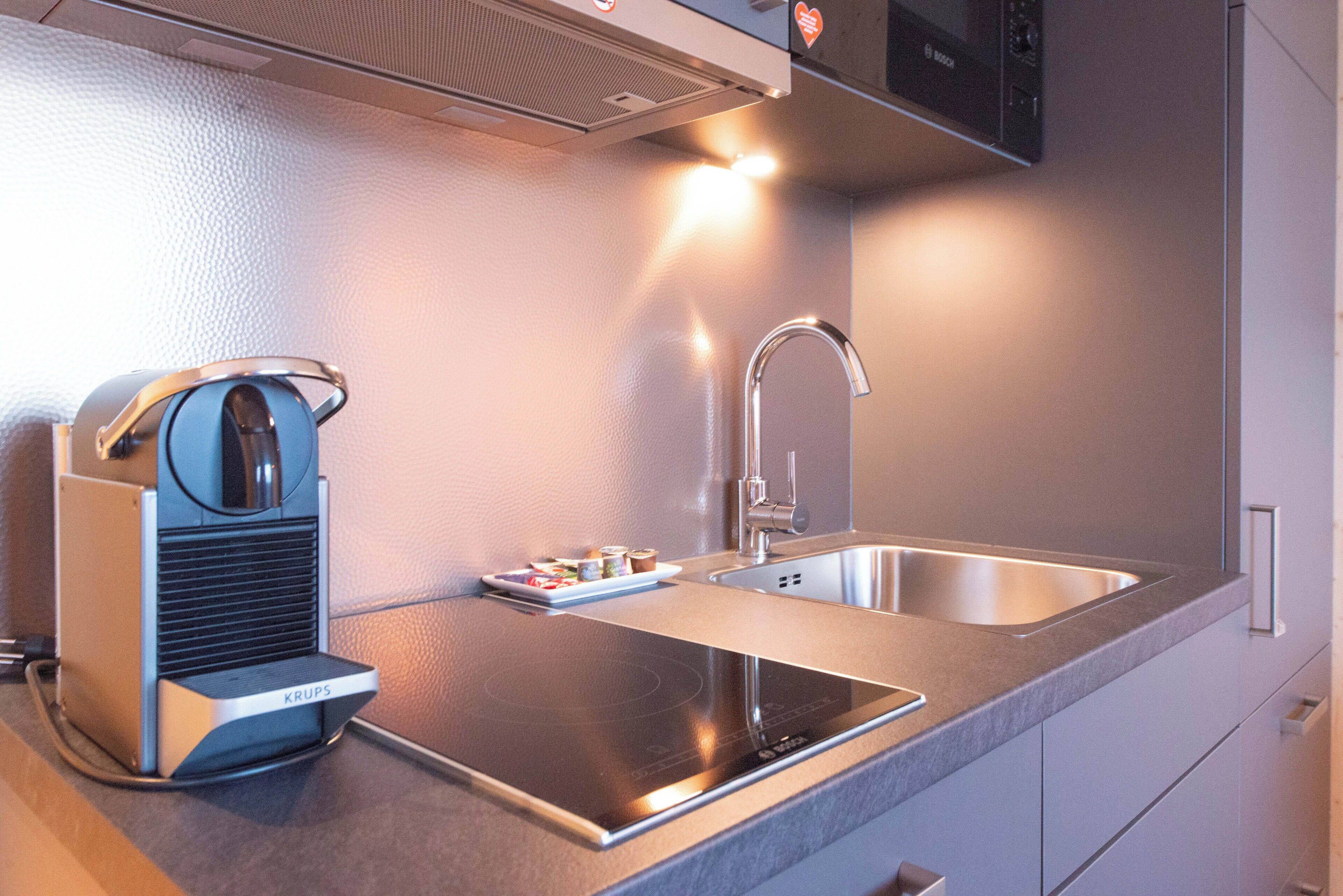 A modern kitchen with a built-in induction cooktop, a stainless steel sink, and a compact coffee machine.