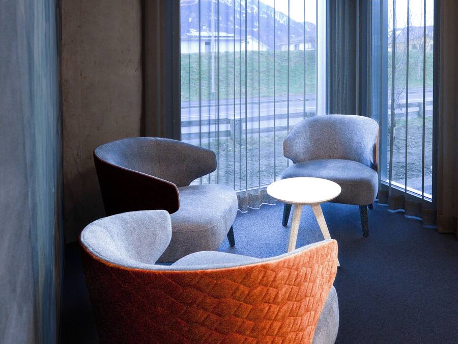A modern hotel room with a large window, two armchairs, a small round table, and a unique circular light fixture.