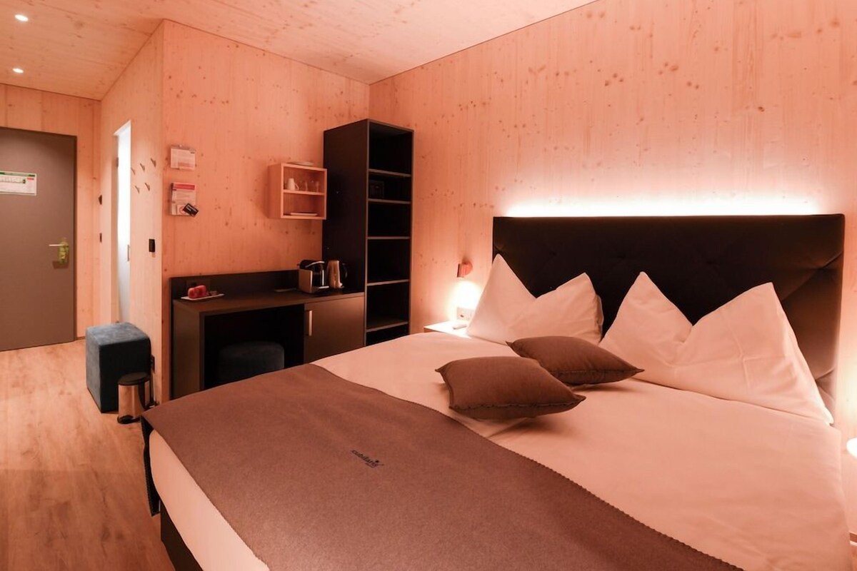 A room with a bed, a desk, a chair, and a shelf unit.