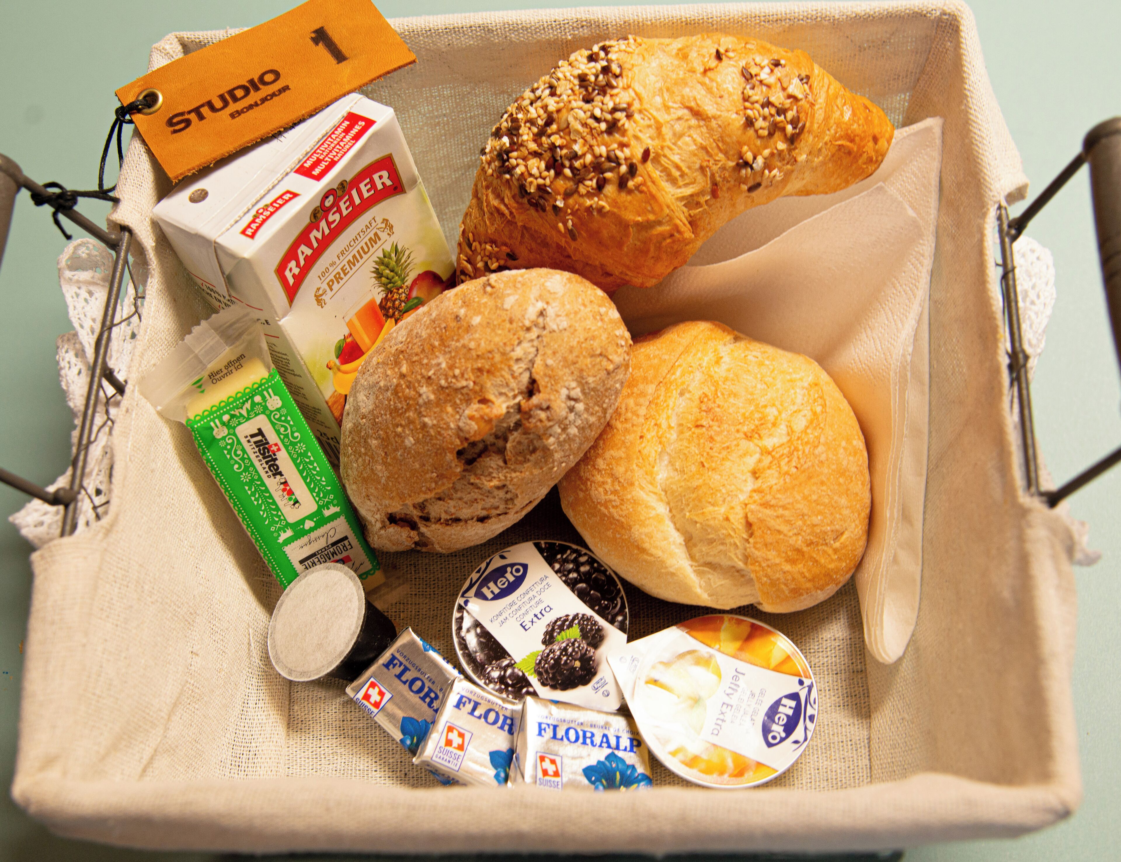 A basket containing a loaf of bread, a pastry, a box of milk, and several chocolate bars.
