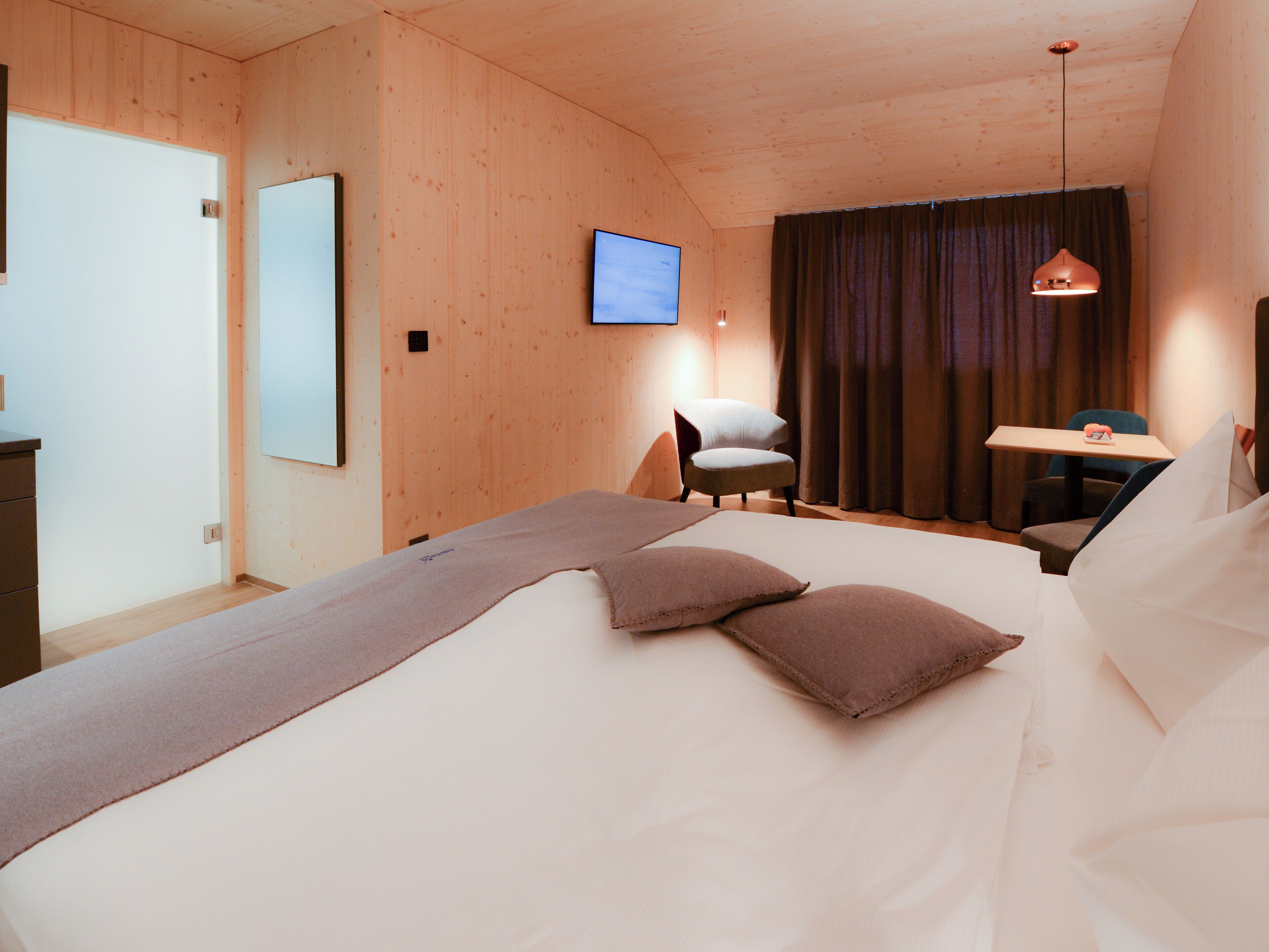 A bedroom with a bed, a chair, a desk, a television, and a window with curtains.