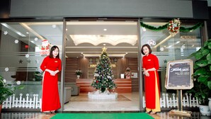 A hotel lobby with a Christmas tree, reception desk, and two staff members in red uniforms. - Binh Minh Hotel (Dong Van)