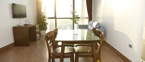 Un comedor moderno con una mesa de vidrio, sillas de madera, una planta en maceta y un televisor en la pared.