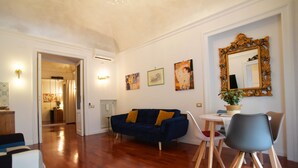 A living room with a dark blue sofa, wooden floor, and a dining area with a white table and chairs. - ♡♡♡ Norma ♡♡♡ (Roma)