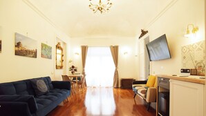 A modern living room with a dark blue sofa, a dining area with a table and chairs, a kitchen with a dishwasher, and a TV mounted on the wall. - ♡♡♡ Norma ♡♡♡ (Roma)