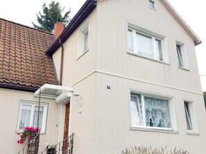A two-story building with a beige facade, a brown tiled roof, and a small porch with a hanging flower basket. - Apartment on Staufenberg (Blankenburg (Harz))
