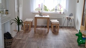 A room with a glass table, wooden floor, white walls, a radiator, a window with curtains, a chair, and a green toy. - Apartment on Staufenberg (Blankenburg (Harz))