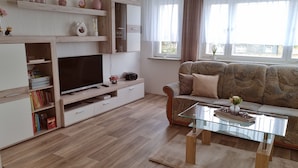 A modern living room with a flat-screen TV, wooden shelves, a sofa, and a glass coffee table. - Apartment on Staufenberg (Blankenburg (Harz))