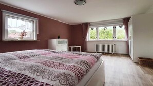 A bedroom with a large bed, a dresser, a radiator, and a window with curtains. - Apartment on Staufenberg (Blankenburg (Harz))