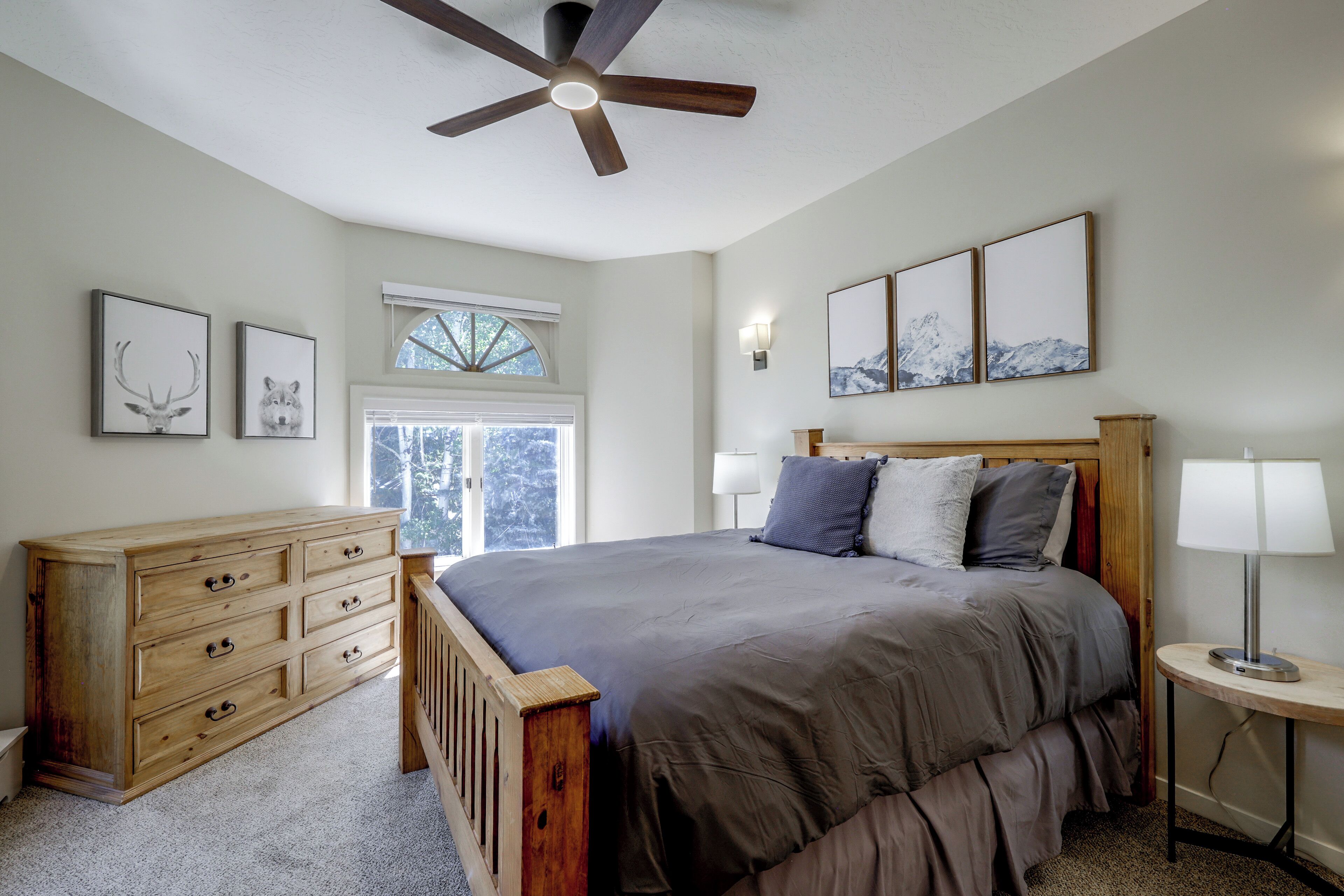 A bedroom with a wooden bed, a ceiling fan, a dresser, a window, and wall-mounted artwork.