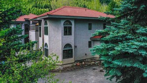 A two-story house with a red-tiled roof, surrounded by lush greenery and a mountainous backdrop. - Townhome ~ 4 Mi to Beaver Creek & 8 Mi to Vail! (Avon)