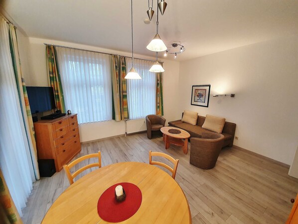 Ein Wohnzimmer mit einer Couch, Sesseln, einem Couchtisch, einem Fernseher und einem Holzschrank.