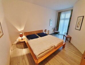 A hotel room with a wooden bed, a chair, a table, and a window with curtains.