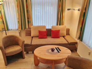 A cozy living room with a sofa, two red cushions, a wooden coffee table, and a chair.