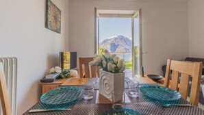 A dining area with a table set for two, a vase with flowers, and a view of mountains through an open door. - Palma Romantic Dream (Perledo)