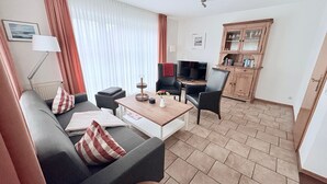 Una sala de estar moderna con un sofá, una mesa de centro y un televisor. Se observa un mueble de madera y una lámpara.