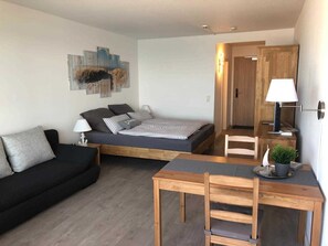 A compact bedroom with a bed, bedside table, lamp, and a small potted plant.