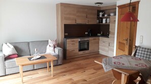Un espacio habitable compacto con kitchenette, un sofá, una mesa de comedor y un cojín estampado en una silla.