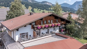Un chalet doté d’un toit en pente, d’un balcon orné de jardinières et offrant une vue sur les montagnes.