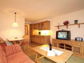 A compact living space with a sofa, a dining table, a kitchen area, and a television.