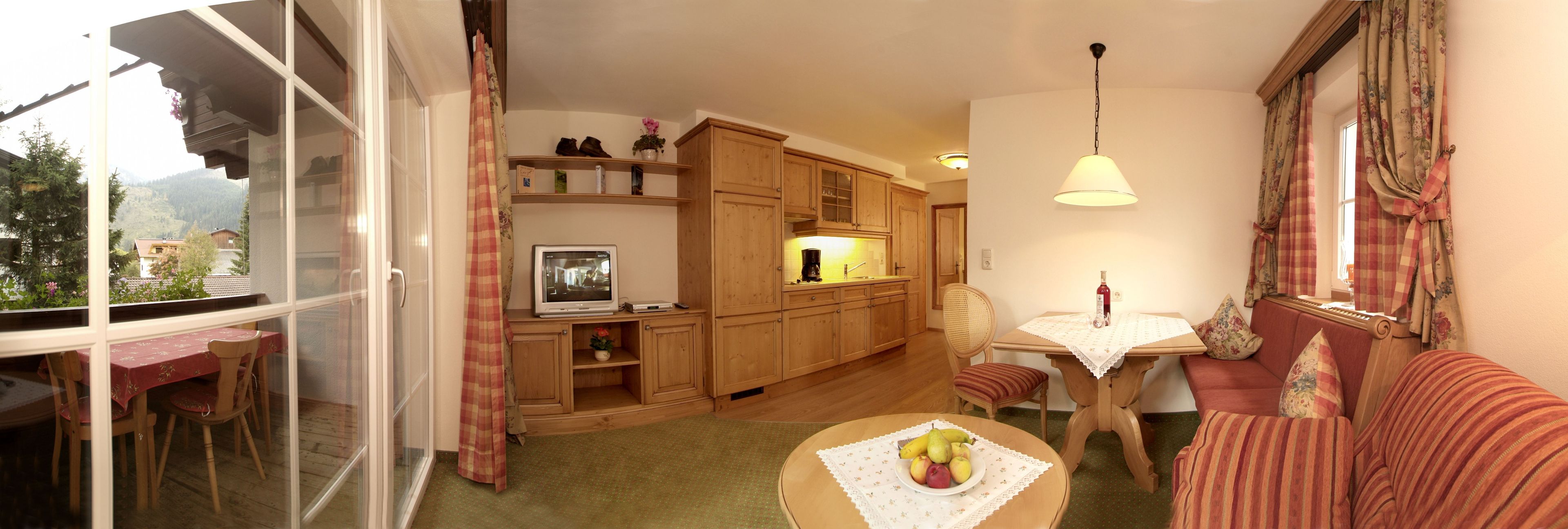 Uma sala de estar aconchegante com área de jantar, armários de madeira, televisão e uma mesa com frutas.