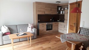Un espace de vie compact comprenant un coin cuisine, un canapé, une table à manger et un plaid à motifs sur une chaise.