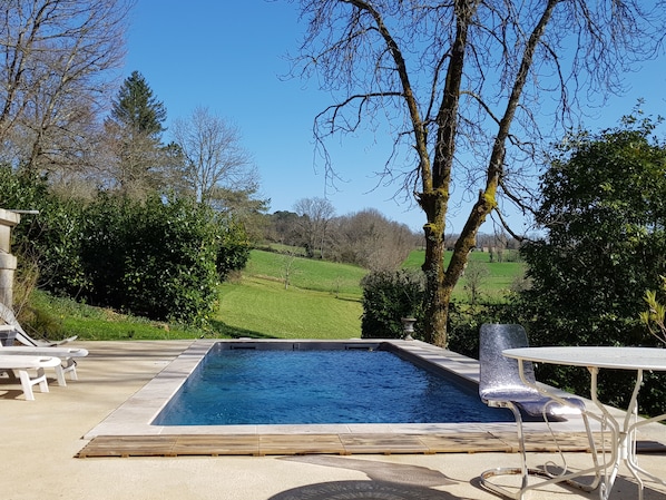 A rectangular swimming pool with a wooden deck in the foreground, surrounded by lounge chairs and a table.